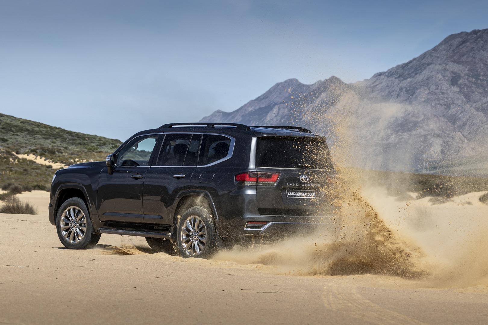 A black land cruiser driving thru the sand